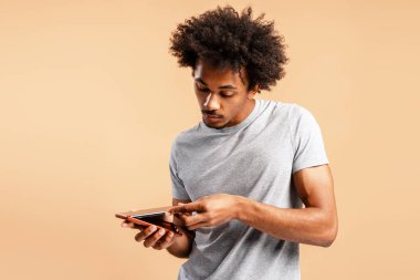 Yakışıklı, Afro-Amerikan bir adam bej arka planda izole edilmiş akıllı telefon için kahverengi telefon kılıfı tutuyor. Güvenlik kavramı