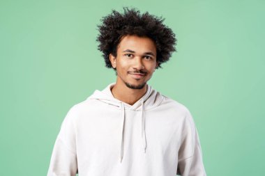Yeşil arka planda izole edilmiş şık bir kapüşonlu giyen, gülümseyen, Afro-Amerikan bir adamın portresi. Mutlu erkek kameraya bakıyor. Reklam kavramı