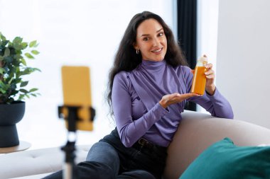 Sosyal medya takipçilerine akıllı telefonuyla içerik kaydedilirken sağlıklı bir içecek sunan bir kadın