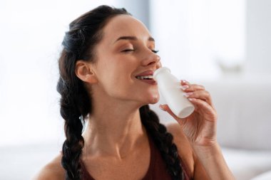 Gözleri kapalı, sağlıklı bir yoğurdun tadını çıkaran genç bir kadın mide sağlığını, refahını ve dengeli bir yaşam tarzını ön plana çıkarıyor.