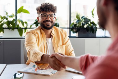 Modern bir ofiste iki farklı adam el sıkışıyor başarılı bir iş anlaşmasını ve ortaklığı kutluyorlar.