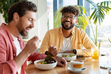 İki farklı arkadaş, modern bir restoranda kahkaha ve sağlıklı bir yemek paylaşıyor, bir arkadaşlık ve beraberlik anı yaratıyor.