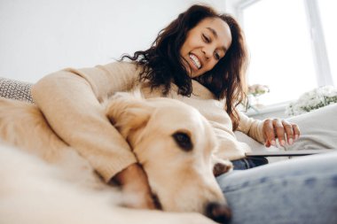Gülümseyen otantik Afro-Amerikan kadın evcil köpek, rahat koltukta oturan Golden Retriever dizüstü bilgisayar. Aşk, evcil hayvan konsepti