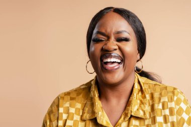 Geniş bir gülümsemesi ve kapalı gözleri olan siyah bir kadın bej bir geçmişi olan gerçek bir duygu ve mutluluk gösteriyor.
