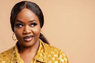 Yüzü şen şakrak, sarı kareli gömlek ve halka küpeli siyah bir kadın yan tarafa bakıyor.