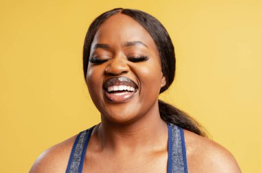 Afro-Amerikalı kadın neşeyle gülüyor, eğleniyor ve gözlerini kapıyor.