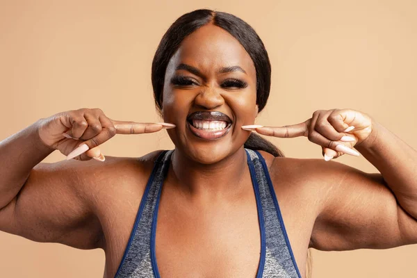 Siyah ve cüsseli bir kadın gülümsüyor, dişlerini gösteriyor, gülümsemesini gösteriyor, vücudunun pozitifliğini ve mutluluğunu destekliyor