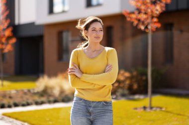 Yeni evinin önünde kolları çapraz duran genç bir ev sahibi.