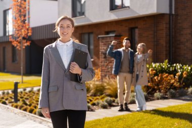 Mutlu çift yeni ev alırken dışarıda duran gülümseyen emlakçı.