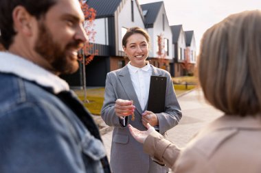 Emlakçı banliyödeki evlerin önünde duran yeni ev sahiplerine anahtarları veriyor.