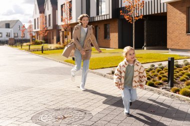 Anne ve kızı güz boyunca modern bir konut kompleksinin sokaklarında mutlu bir şekilde koşuyorlar.