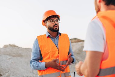 Turuncu yelek ve kask giyen ciddi iş arkadaşları taş ocağındaki maden planlama projesinde konuşuyorlar. Takım çalışması konsepti