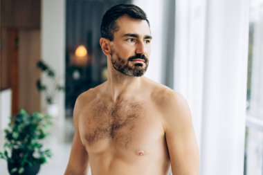 Sakallı, gömleksiz bir adam başka tarafa bakıyor, hayatı düşünüyor ve düşünüyor.