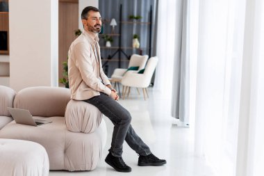 Parlak bir oturma odasında, modern bir kanepede dinlenen bir adam...