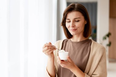 Yoğurt yiyen, gülümseyen ve sağlıklı ve besleyici atıştırmalıkların tadını çıkaran bir kadın.