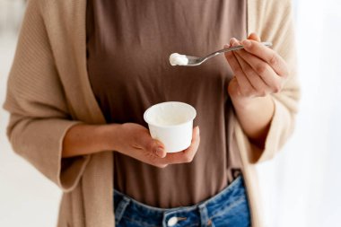 Kadın elleri yoğurt ve kaşık tutuyor, sağlıklı süt ürünlerinin tadını çıkarıyor.