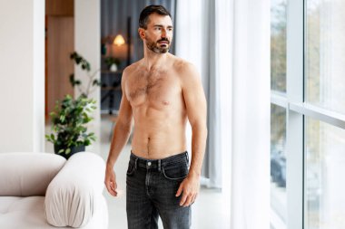 Sakallı adam üstsüz, düşünceli ve düşünceli görünüyor.