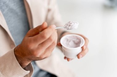 Plastik bardaktan yoğurt yiyen kişi, sağlıklı bir atıştırmalık veya kahvaltı sunar.
