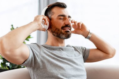 Gözleri kapalı bir adam kanepeye uzanıyor, kulaklıkla müzik dinliyor.