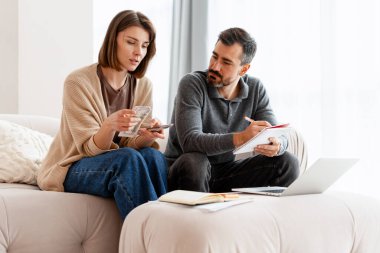 Çift kanepeye oturup ev bütçesi planlıyor ve dizüstü bilgisayarla para sayıyor.