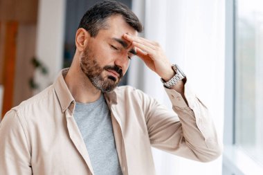 Yorgunluk ve rahatsızlık hisseden bir adam, acıdan alnına dokunur.