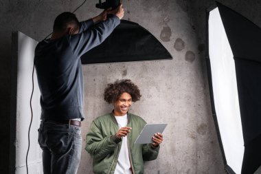 Profesyonel bir stüdyo fotoğraf çekimi sırasında işbirliği yapan iki adam. Tabletteki resimleri inceleyen genç bir yaratıcı model.