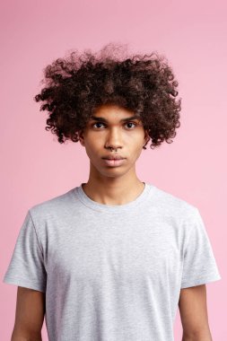 Kıvırcık saçlı genç adam pembe arka planda duruyor. Bireyselliğini ve Z jenerasyonunu gösteriyor.