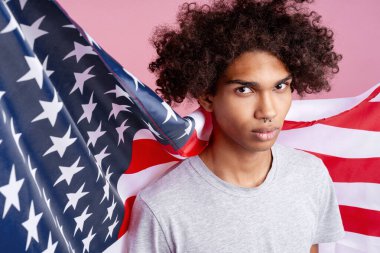 Afro saçlı ve burnunda piercing olan genç bir adam. Amerikan bayrağı taşıyor. Vatanseverlik, birlik ve ulusal kimliği temsil ediyor.