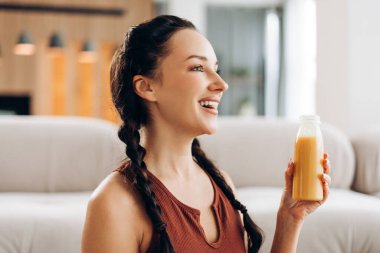 Sütyen giyen, elinde portakal suyu olan güzel, neşeli bir kadın evde, oturma odasında gözlerini kaçırıyor. Sağlık yaşam tarzı kavramı