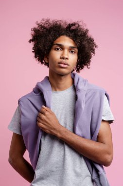 Pembe arka planda izole edilmiş şık bir kapüşonlu giyen çekici Latin adamın portresi. Moda mankeni stüdyoda kameraya bakıyor. Reklam kavramı