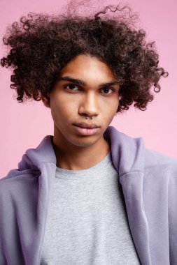 Pembe arka planda izole edilmiş şık bir kapüşonlu giyen yakışıklı Latin adamın portresi. Moda mankeni stüdyoda kameraya bakıyor. Reklam kavramı