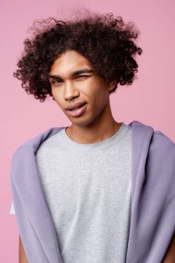 Burnunda piercing olan düşünceli, yakışıklı Afro-Amerikan bir adam kameraya bakıyor, pembe arka planda izole edilmiş bir şekilde poz veriyor. Reklam kavramı