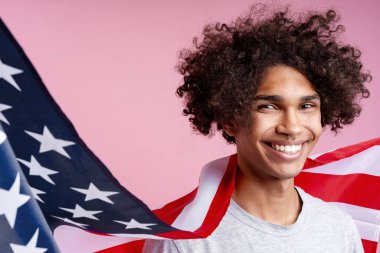 Amerikan bayrağı tutan mutlu Afro-Amerikan bir adamın portresi pembe arka planda izole bir şekilde uzağa bakıyor. 4 Temmuz, bağımsızlık günü konsepti