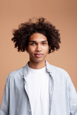 Gülümseyen, heyecanlı, burnu delik, günlük kıyafetler giyen, bej arka planda izole edilmiş kameraya bakan Afro-Amerikan genç adam. Reklam kavramı