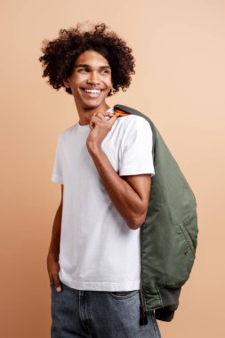 Gülümseyen, burnu delinmiş, yeşil ceketli yakışıklı Afro-Amerikalı adam bej arka planda yalnız poz veriyor. Reklam alışverişi konsepti