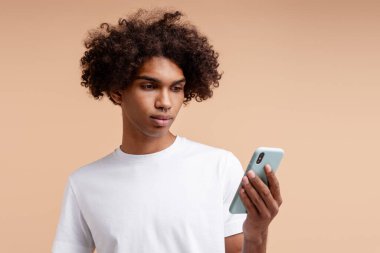 Dalgın, ciddi kıvırcık kıvırcık saçlı, burnunda cep telefonu olan, bej arka planda sohbet eden Amerikalı bir adam. Çevrimiçi teknoloji kavramı