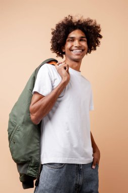 Burnuna piercing takan, yeşil ceket giyen, bej arka planda yalnız poz veren yakışıklı Afro-Amerikan bir adam. Reklam alışverişi konsepti