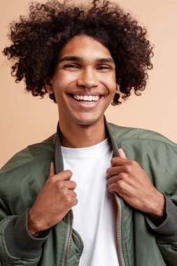 Gülümseyen mutlu Afro-Amerikalı genç adamın yakın plan portresi. Burnu delinmiş, gündelik modern ceket giymiş, bej arka planda izole edilmiş poz veriyor. Reklam, alışveriş konsepti