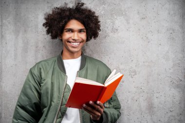 Turuncu not defteri tutan şık yeşil ceketli gülümseyen Afrikalı Amerikalı adamın portresi gri arka planda izole edilmiş kameraya bakıyor. Eğitim kavramı