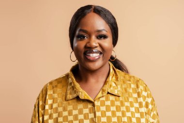 Gülümseyen Afro-Amerikan modeli bej arka planda yalnız poz veren kameraya bakıyor. Stüdyoda manken. Reklam, güzellik konsepti