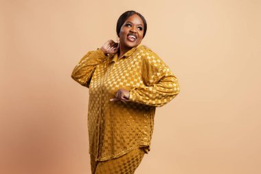 Mutlu, neşeli, Afro-Amerikan artı beden modeli şık günlük kıyafetler giyiyor ve bej arka planda yalnız dans ediyor. Eğlenceli konsept