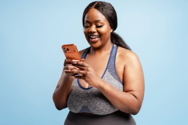 Gülümseyen, artı boy Afro-Amerikan kadın elinde cep telefonu olan cep telefonu uygulaması mesajını mavi arka planda izole etmiş. Çevrimiçi teknoloji kavramı