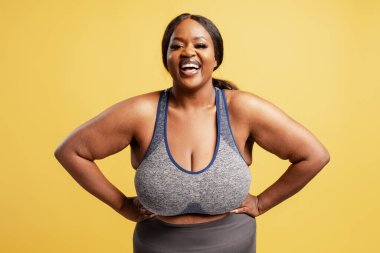 Gülümseyen mutlu portresi artı Afrikalı Afrikalı Amerikalı kadın şık giyinmiş kameraya bakıyor, sarı arka planda izole poz veriyor. Spor, antrenman konsepti