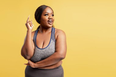 Güzel Afro-Amerikan artı beden modeli şık spor giysiler giyiyor sarı arka planda izole edilmiş fotokopi alanına bakıyor. Reklam alışverişi konsepti