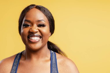 Sarı arka plan fotokopi alanında izole edilmiş kameraya bakan gülümseyen Afro-Amerikan kadın portresi. Reklam kavramı