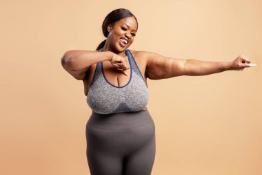 Bej arka planda izole edilmiş spor giysiler giyen gülümseyen Afro-Amerikan kadın portresi. Eğitim kavramı