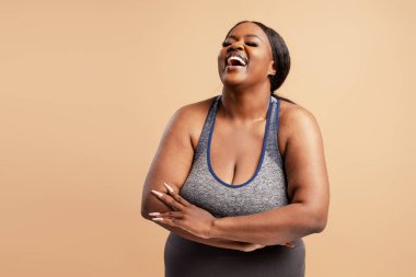 Güzel, gülümseyen, pozitif Afro-Amerikan kadın şık giyinmiş bej arka planda izole bir şekilde kahkaha atıyor. Pozitif yaşam tarzı kavramı