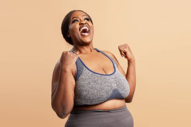 Mutlu, gülümseyen Afro-Amerikan kadın kutlama kıyafetleri giyerek bej arka planda izole edilmiş para kazanıyor. Zafer konsepti