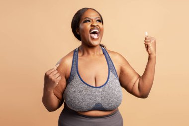 Neşeli, gülümseyen Afro-Amerikan kadın kutlama kıyafetleri giyerek bej arka planda izole edilmiş para kazanıyor. Zafer konsepti