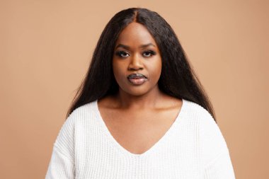 Bej arka planda izole edilmiş kameraya bakan uzun siyah saçlı dalgın, iri yapılı Afro-Amerikan kadının portresi. Güzellik konsepti
